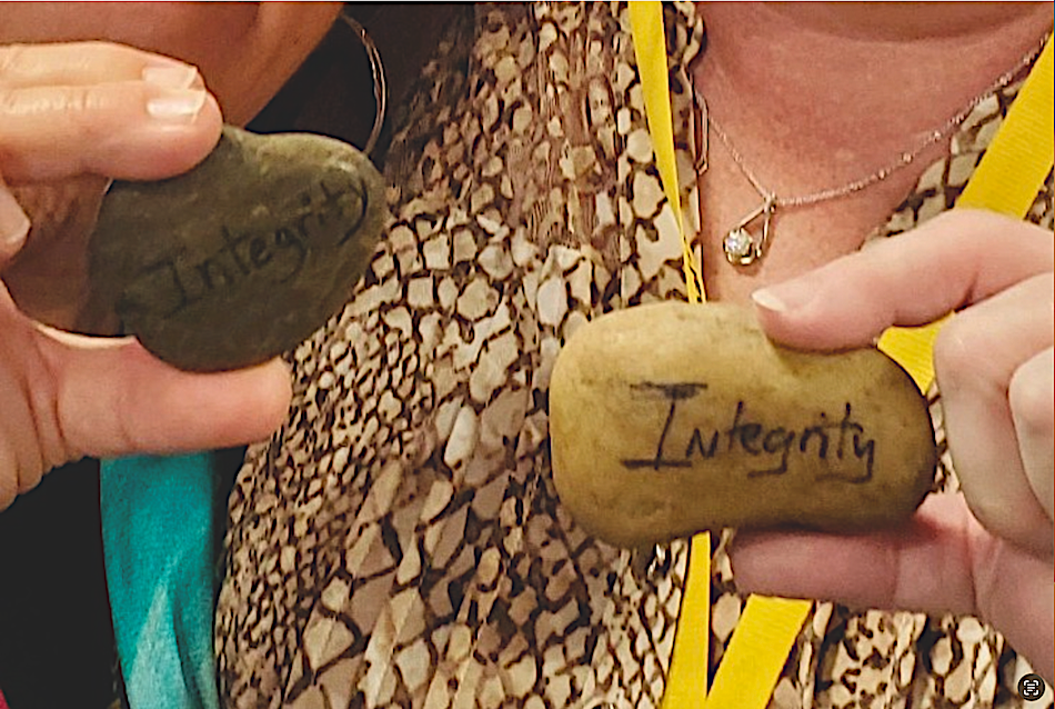 Hands holding one rock each with the word "Integrity" painted on each rock.