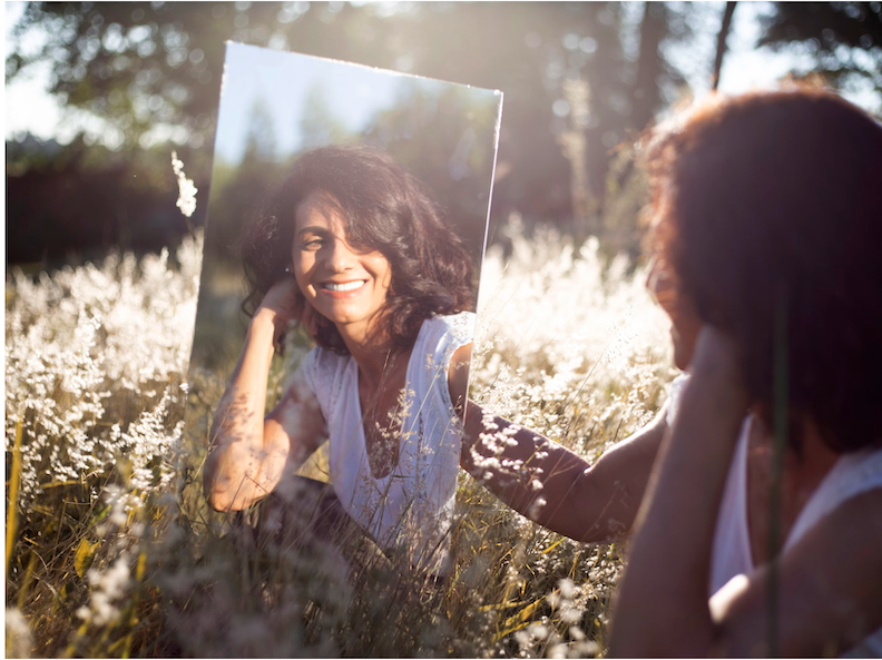 Woman looking in mirror while sitting in a field