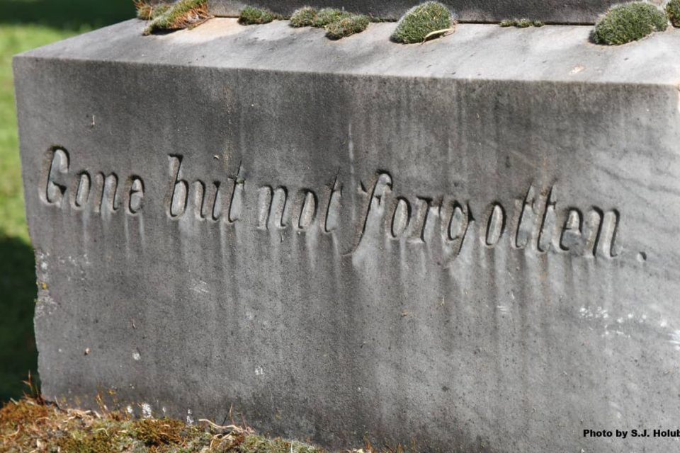 An old headstone in a graveyard with the words, "Gone but not forgotten" inscribed in the stone