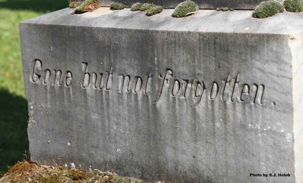 An old headstone in a graveyard with the words, "Gone but not forgotten" inscribed in the stone