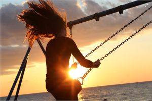 Woman swinging on a swingset at sunset.