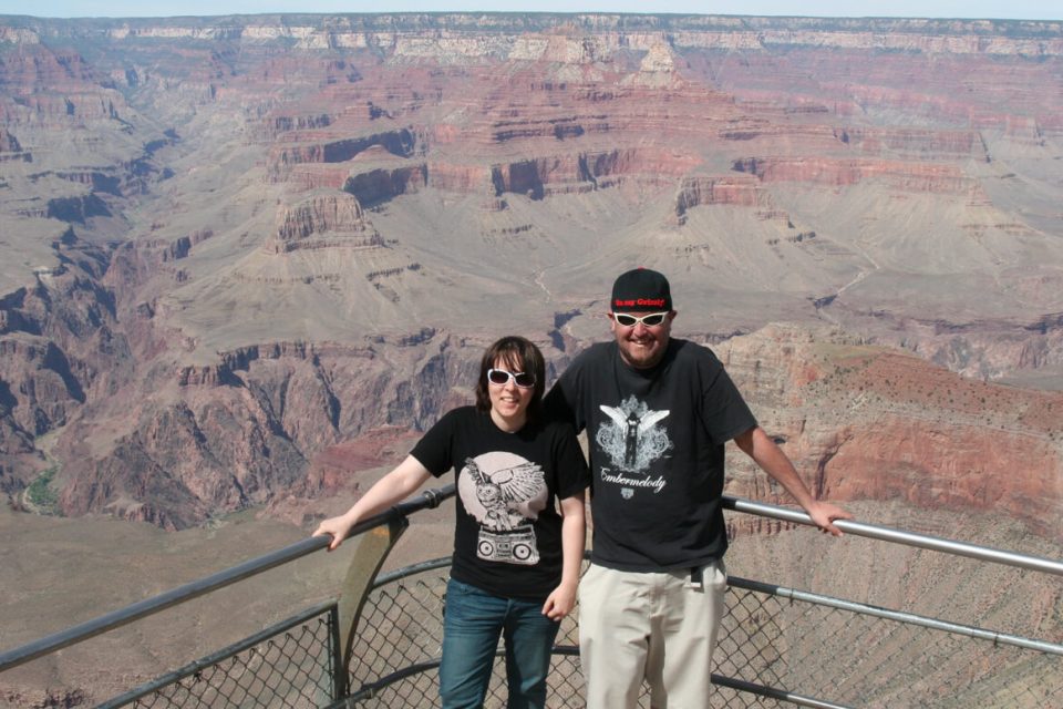 A couple stands in front of the railing of the grand canyon