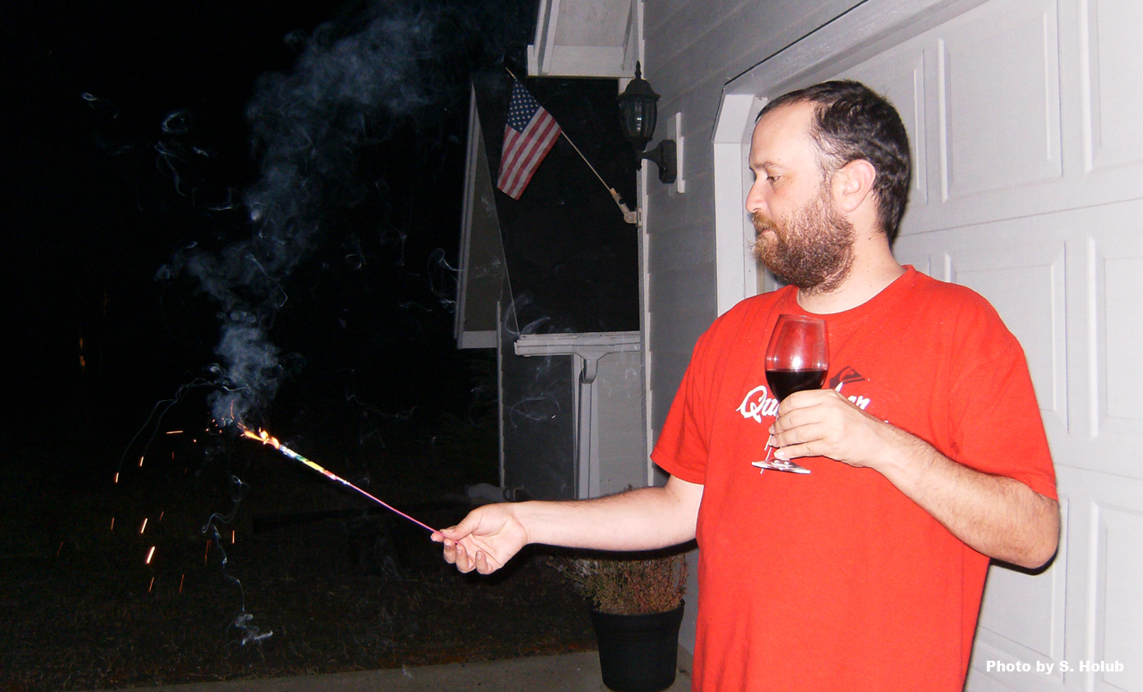 a man holds a wine glass and a sparkler on 4th of July