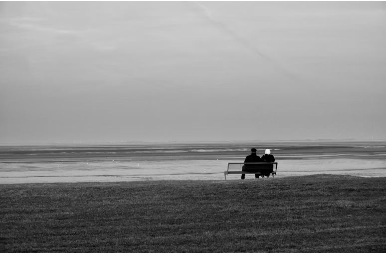 Two people sitting on a bench facing an ocean.