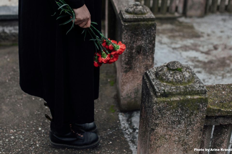 a view of the lower half of a person with focus on the hand holding red flowers in a graveyard
