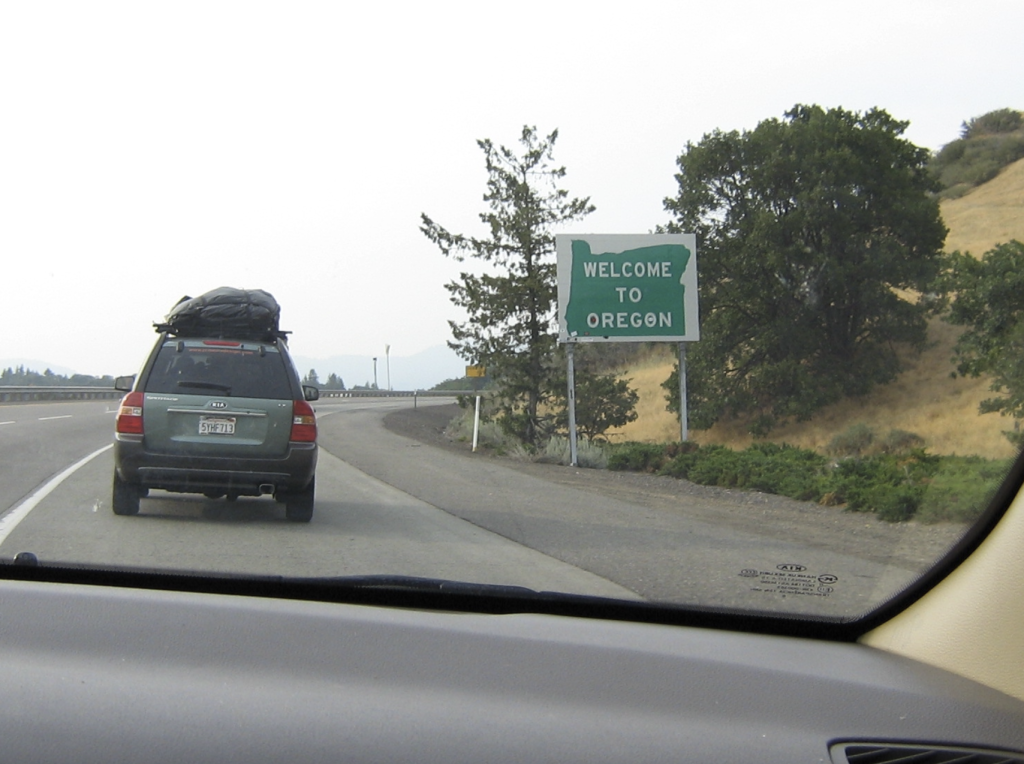A green SUV by the Welcome to Oregon sign on the freeway