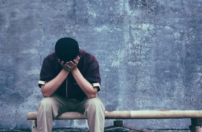Man with head in hands, crying while sitting on a bench.