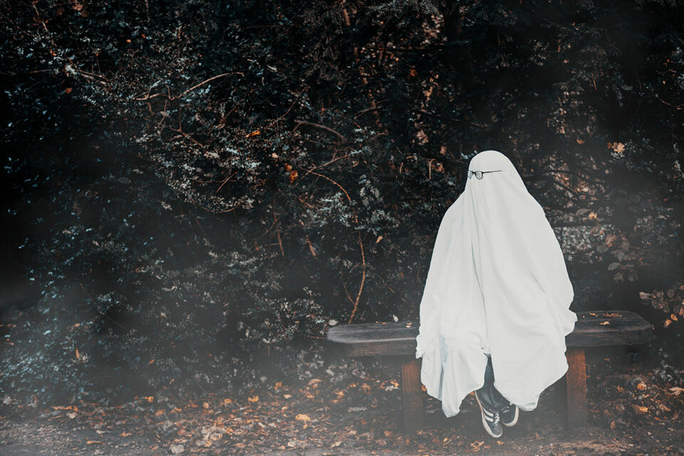a person sitting on a bench dressed as a ghost