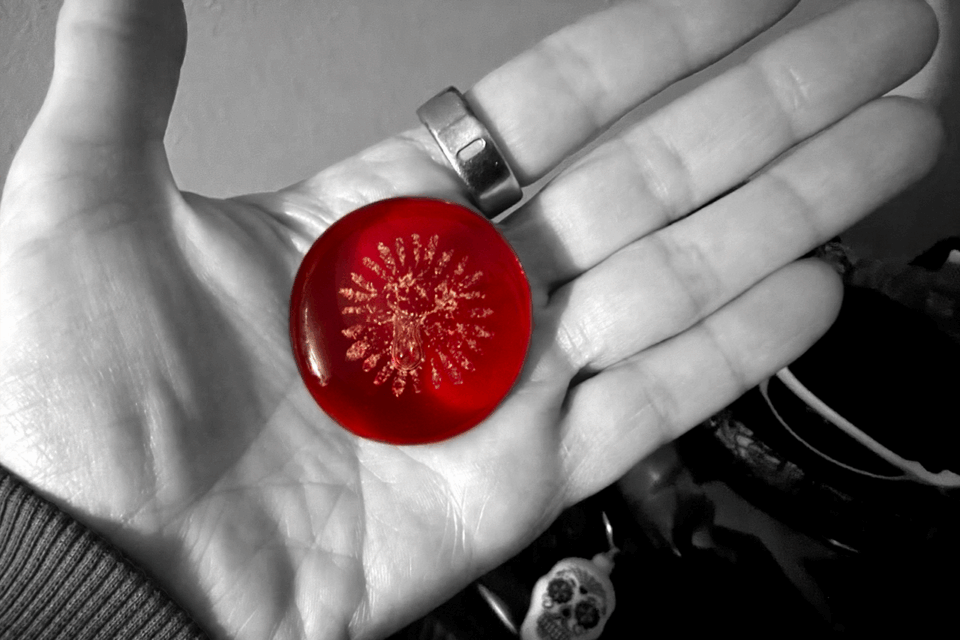 a hand holding a red "Bobrock" artisan glass keepsake with ashes