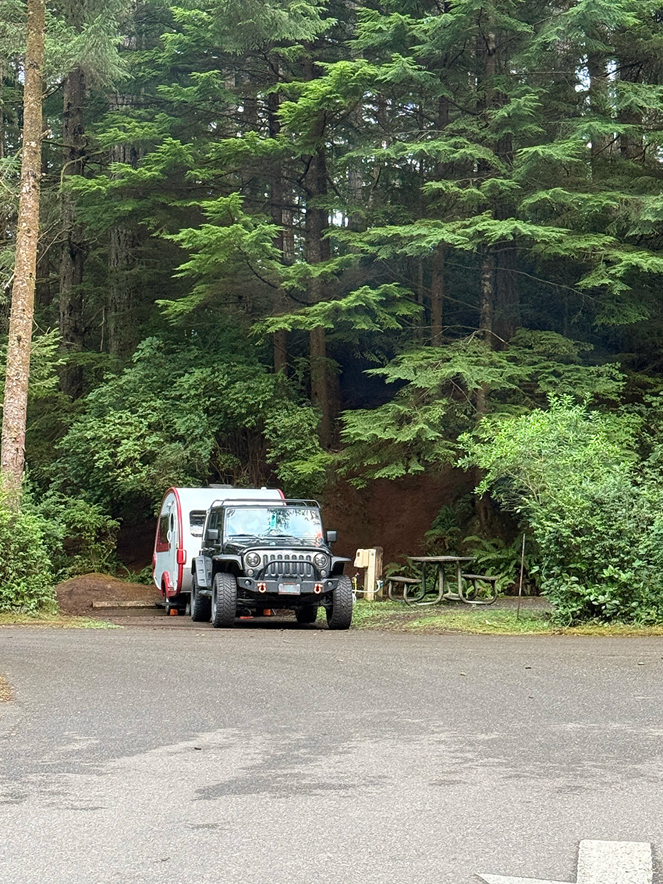 A Jeep and a teardrop trailer backed into a camp spot at a state park in Oregon.